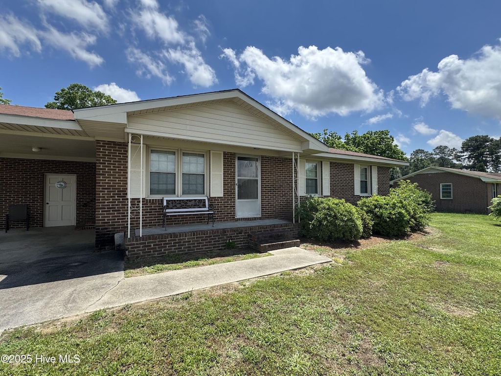 ranch-style home with a front yard, brick siding, an attached carport, concrete driveway, and covered porch