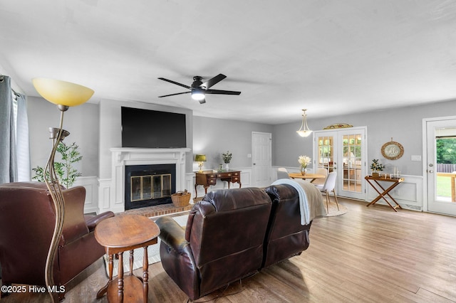 living room featuring a glass covered fireplace, a ceiling fan, wainscoting, a decorative wall, and light wood-type flooring