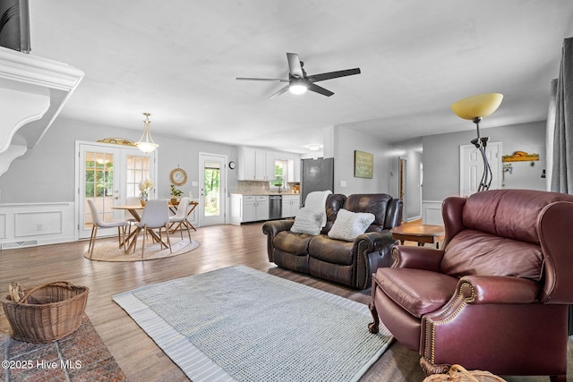 living area featuring a ceiling fan, wainscoting, and wood finished floors
