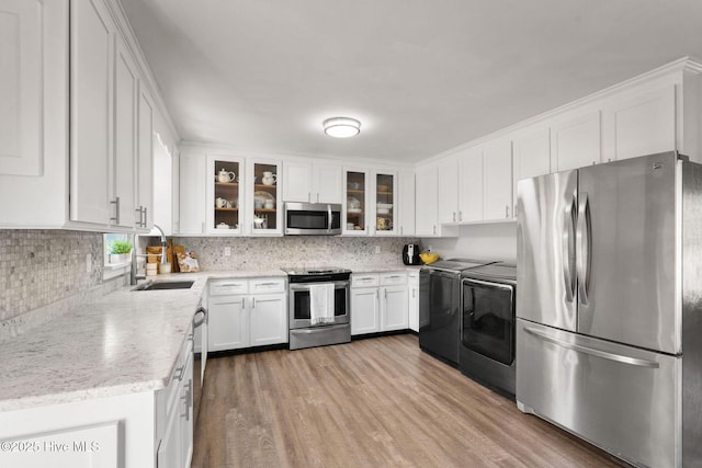 kitchen featuring appliances with stainless steel finishes, washing machine and dryer, a sink, white cabinets, and wood finished floors