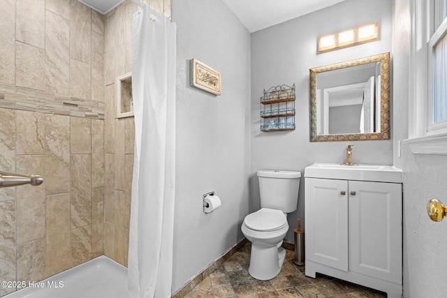 bathroom featuring toilet, a tile shower, baseboards, vanity, and stone finish floors