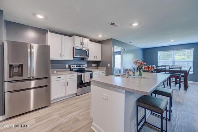 1145 Saint Augustine Dr, Castle Hayne, NC 28429 - kitchen featuring appliances with stainless steel finishes, light wood-type flooring, a sink, white cabinetry, and a breakfast bar