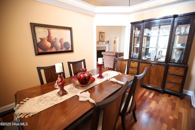 dining space with wood finished floors, crown molding, a fireplace, and baseboards
