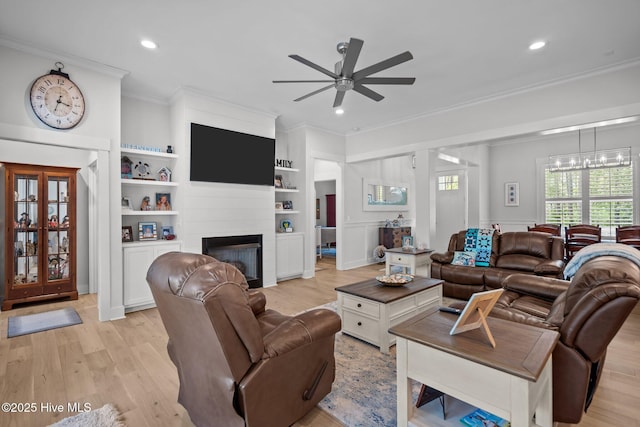 living room featuring ornamental molding, a ceiling fan, light wood-style flooring, a glass covered fireplace, and recessed lighting