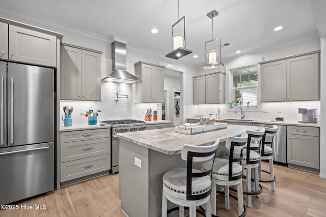 kitchen featuring high quality appliances, wall chimney exhaust hood, gray cabinets, a sink, and crown molding