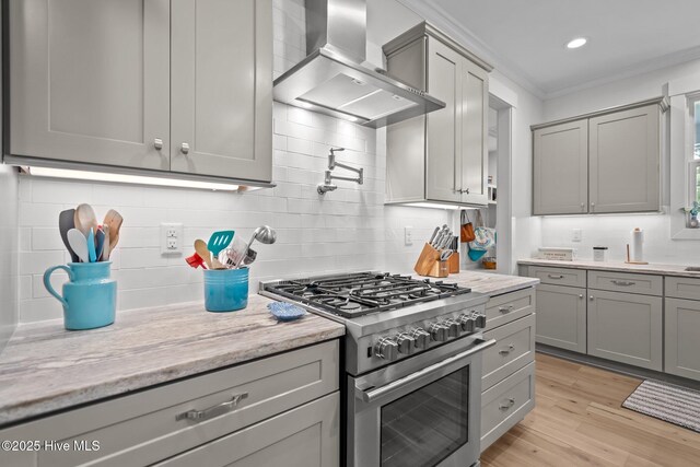 kitchen featuring high end range, wall chimney range hood, gray cabinets, backsplash, and ornamental molding