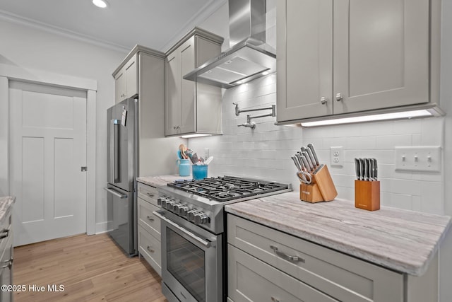 kitchen with high end appliances, wall chimney exhaust hood, gray cabinetry, decorative backsplash, and light wood-type flooring