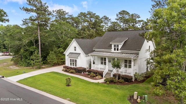 view of front facade with a standing seam roof, covered porch, metal roof, driveway, and a front yard