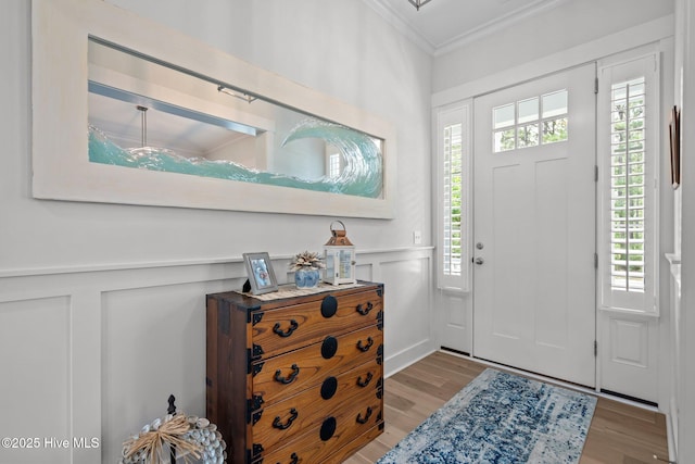 entryway with ornamental molding, light wood finished floors, a decorative wall, and wainscoting