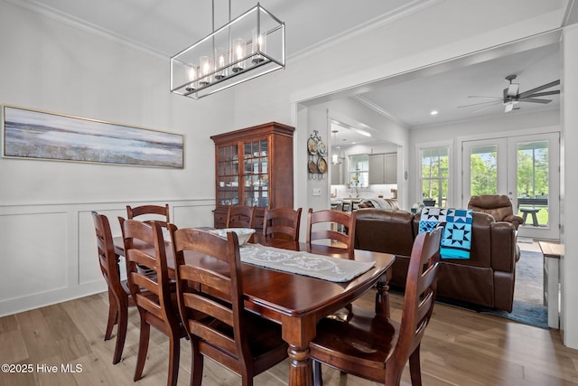 dining room featuring light wood-style floors, crown molding, a wainscoted wall, a ceiling fan, and a decorative wall
