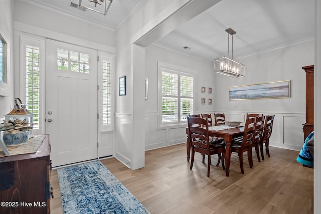 entryway featuring a chandelier, light wood finished floors, a decorative wall, crown molding, and wainscoting