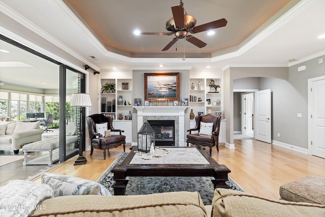 living area featuring ceiling fan, crown molding, a raised ceiling, a premium fireplace, and light wood finished floors