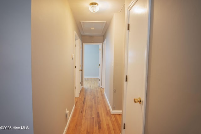 hall featuring attic access, light wood-style flooring, and baseboards