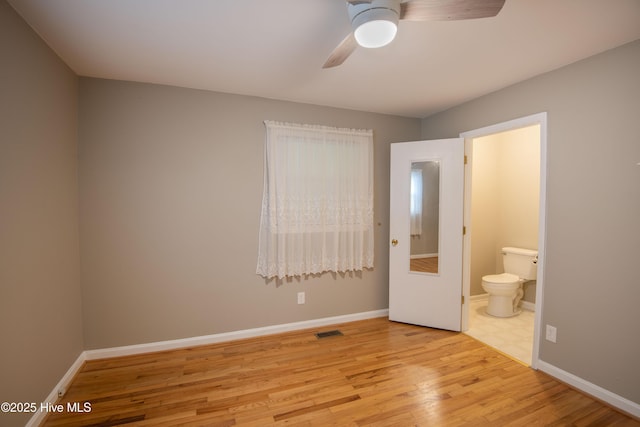 unfurnished bedroom with wood finished floors, ensuite bath, baseboards, and a ceiling fan