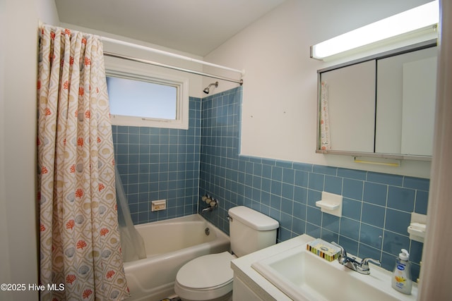 full bathroom featuring shower / bath combination with curtain, a sink, toilet, wainscoting, and tile walls