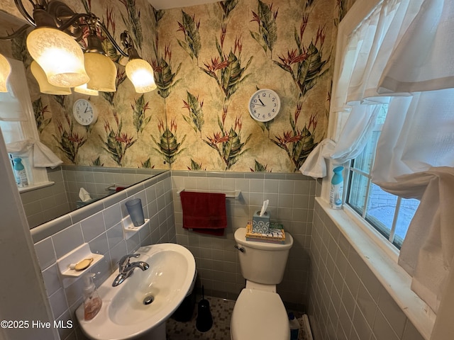 bathroom featuring wallpapered walls, a sink, tile walls, a wainscoted wall, and toilet