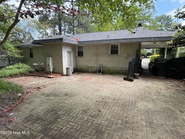 rear view of house featuring brick siding, a shingled roof, an attached carport, and a chimney