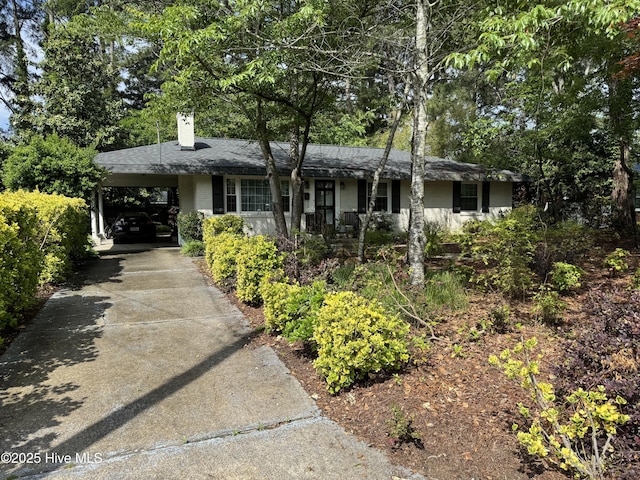ranch-style house with a chimney, concrete driveway, and an attached carport