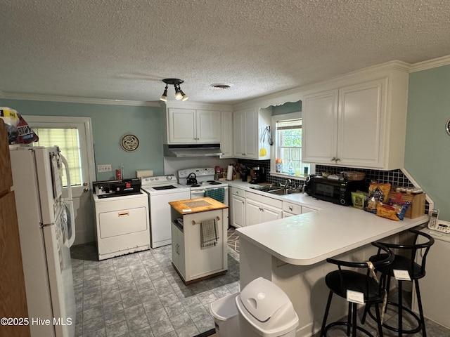 kitchen with independent washer and dryer, white appliances, under cabinet range hood, a peninsula, and a sink