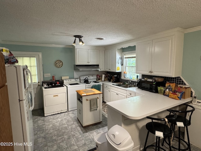 kitchen with separate washer and dryer, white appliances, under cabinet range hood, a peninsula, and a sink