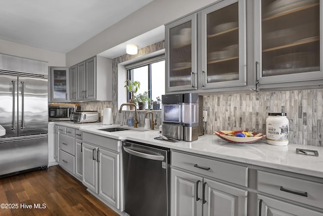 kitchen with stainless steel appliances, a sink, light stone countertops, gray cabinets, and tasteful backsplash