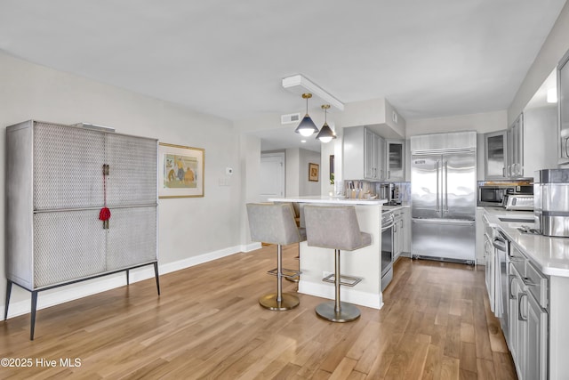 kitchen featuring stainless steel appliances, gray cabinetry, a peninsula, a kitchen breakfast bar, and light wood-type flooring