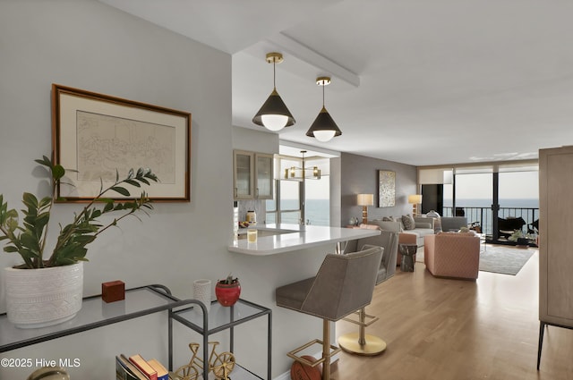 kitchen with a breakfast bar, light wood finished floors, hanging light fixtures, glass insert cabinets, and a wall of windows
