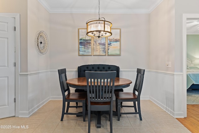 dining area with a chandelier, ornamental molding, a wainscoted wall, and light tile patterned floors