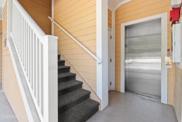stairway featuring wood walls, elevator, and finished concrete flooring