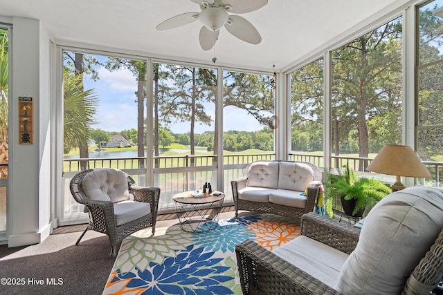 sunroom featuring a ceiling fan, a water view, an outdoor living space, and view of wooded area