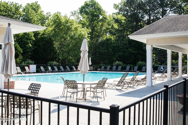 community pool featuring fence, a patio area, and view of wooded area