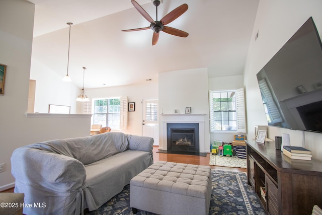 living area featuring a ceiling fan, a fireplace with flush hearth, wood finished floors, and high vaulted ceiling