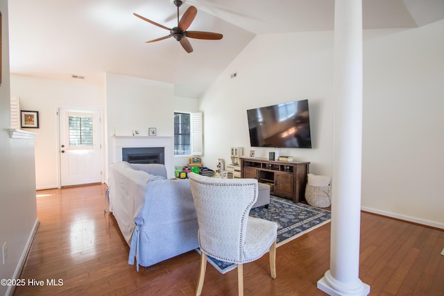 living area with decorative columns, ceiling fan, a glass covered fireplace, wood finished floors, and high vaulted ceiling