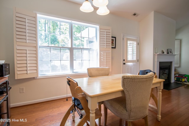 dining area featuring a chandelier, wood finished floors, a glass covered fireplace, and baseboards