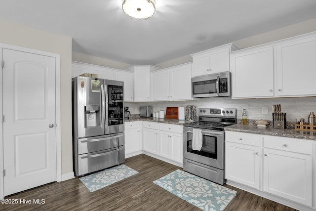 kitchen featuring appliances with stainless steel finishes, white cabinetry, dark wood-type flooring, tasteful backsplash, and dark stone countertops