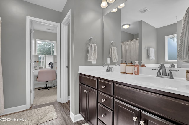 full bath featuring wood finished floors, double vanity, and baseboards