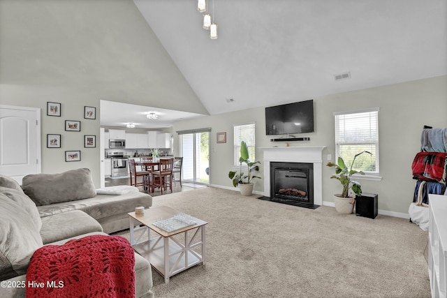 carpeted living area with high vaulted ceiling, plenty of natural light, baseboards, and a fireplace with flush hearth