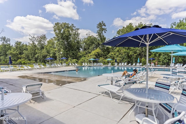 community pool featuring a patio area, fence, and view of wooded area