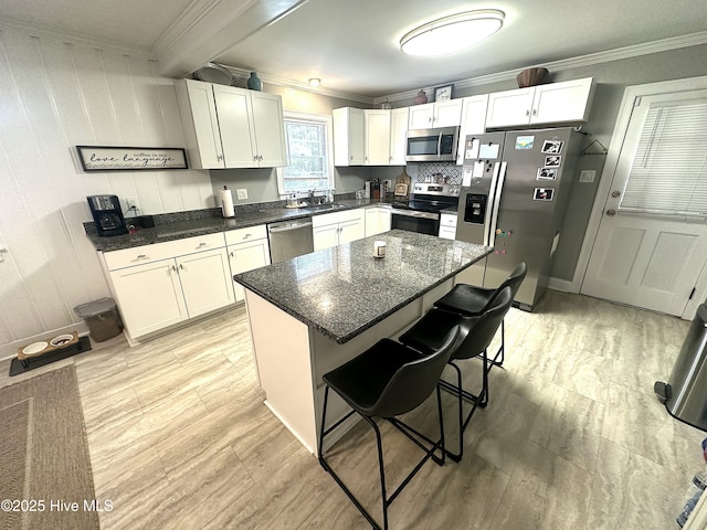 kitchen featuring stainless steel appliances, crown molding, a sink, a breakfast bar, and white cabinets