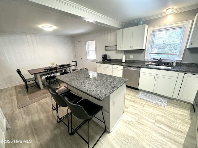 kitchen featuring stainless steel dishwasher, a sink, crown molding, a breakfast bar, and a kitchen island