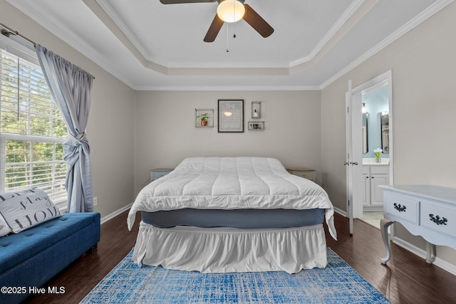 bedroom with a tray ceiling, dark wood-type flooring, ensuite bathroom, a ceiling fan, and ornamental molding