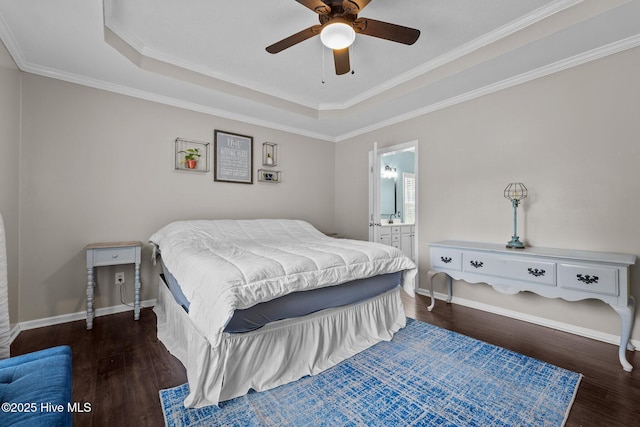 bedroom with wood finished floors, a tray ceiling, crown molding, baseboards, and ensuite bathroom