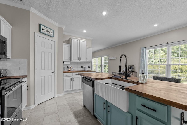 kitchen featuring butcher block counters, appliances with stainless steel finishes, white cabinets, tasteful backsplash, and a textured ceiling