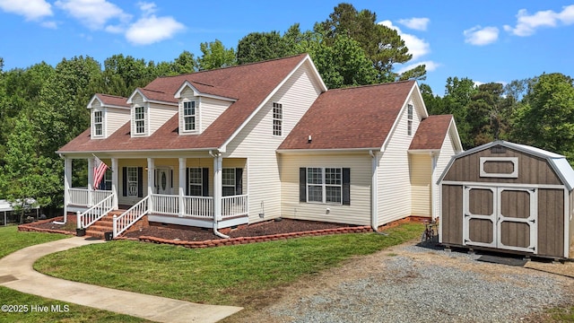 cape cod house featuring a storage unit, covered porch, a front lawn, an outdoor structure, and roof with shingles