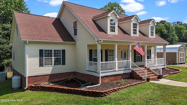 new england style home featuring crawl space, a storage unit, a porch, a front lawn, and an outdoor structure