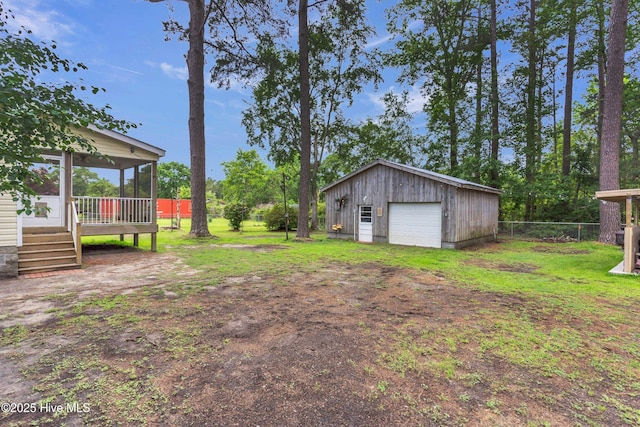 view of yard with a sunroom, a detached garage, dirt driveway, an outdoor structure, and a deck