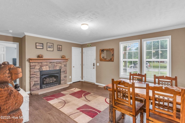 dining space featuring wood finished floors, ornamental molding, a fireplace, baseboards, and a textured ceiling