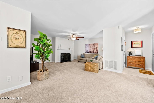 living area featuring carpet floors, a ceiling fan, baseboards, and a fireplace with flush hearth