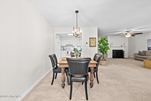 dining room with light colored carpet, baseboards, a chandelier, ceiling fan, and a fireplace with flush hearth