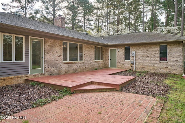 rear view of property featuring a chimney, a deck, brick siding, and a shingled roof
